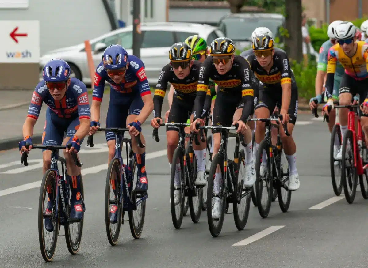 Pelotón de ciclistas en movimiento durante etapa de carrera mostrando cohesión táctica del equipo.