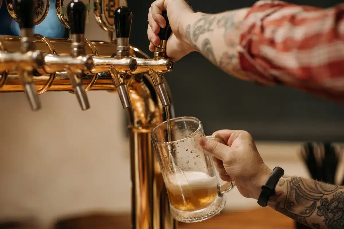 Camarero abriendo un botellero frigorífico lleno de botellas de cerveza en un bar durante el verano