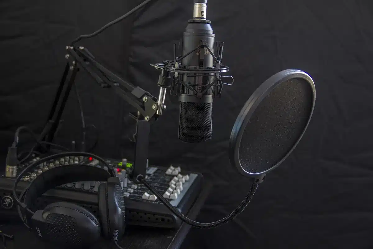 Manos de un técnico junto a un micrófono y guiones en una mesa de radio