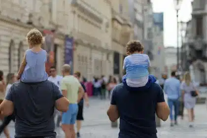 Manos silueteadas y figuras a distancia junto a maletas y un chaleco salvavidas en un paseo costero