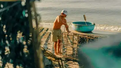 Personas anónimas junto a un espigón y pequeñas barcas en la costa, inspeccionando redes