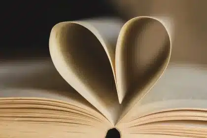 Manos abriendo páginas de un libro en luz suave de biblioteca, con arquitectura vaticana al fondo