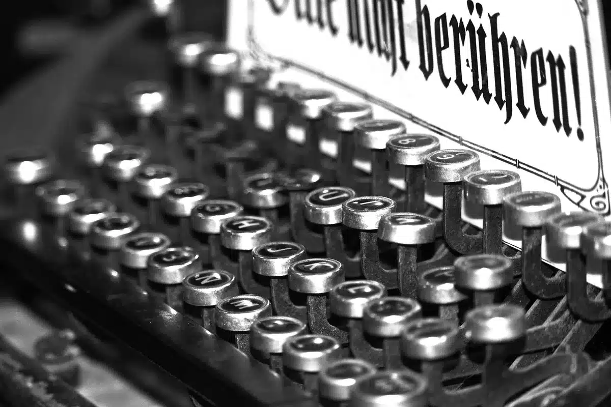Manos de una mujer escribiendo en máquina de escribir rodeada de revistas y papeles en un escritorio