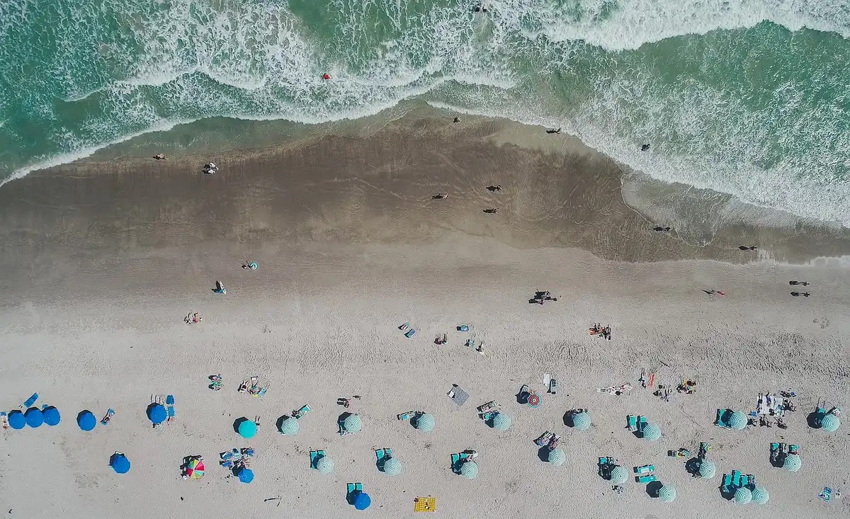 Playa soleada con personas bajo sombrillas en jornada calurosa