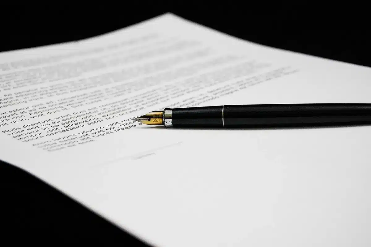 Manos firmando un contrato sobre una mesa, con un bolígrafo y documentos