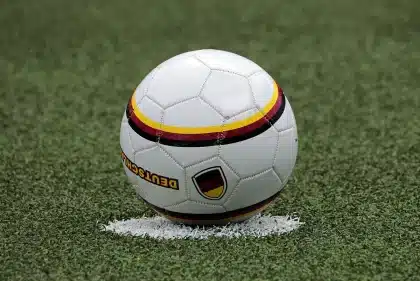 Mujeres celebrando en un campo de fútbol vacío, manos alzadas con una pelota