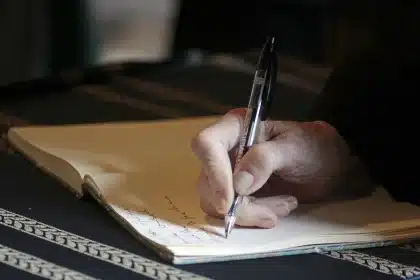 Manos anónimas sobre un manuscrito medieval junto a un escudo en pedestal en exterior